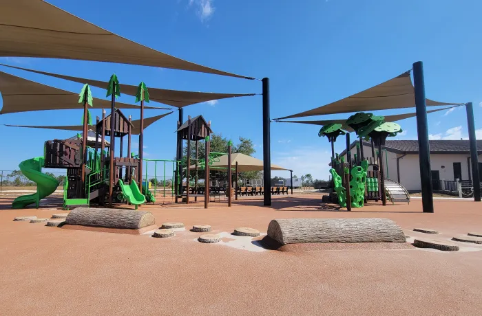 Completed playground by Pro Playgrounds with green slides, shade sails, and log steppers on rubber surface