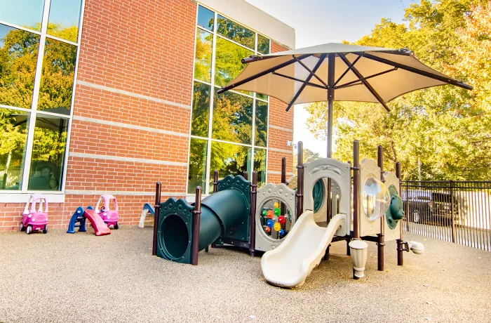 Daycare playground with slides and tunnel under umbrella shade, installed by Pro Playgrounds