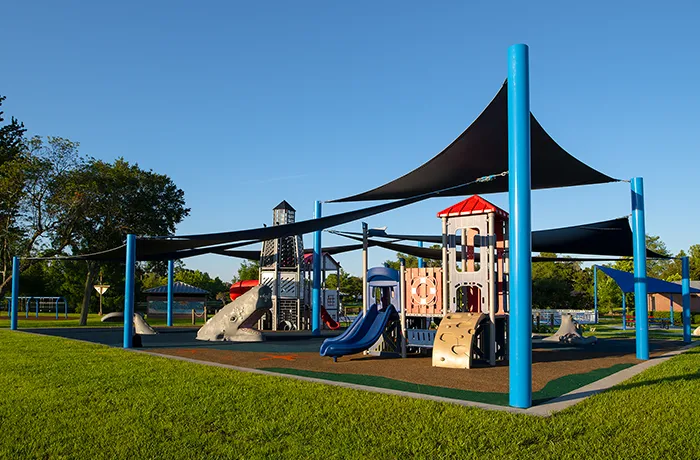 Playground with slides, towers, and shade sails in park, installed by Pro Playgrounds