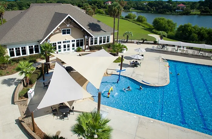 Triangular shade sail structures over community pool and seating area near clubhouse