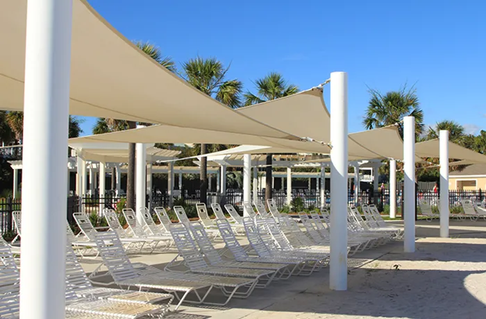 White shade sail canopies over poolside lounge chairs supported by white columns
