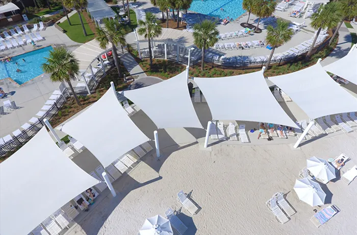 White shade sail structures over resort pool deck with lounge chairs
