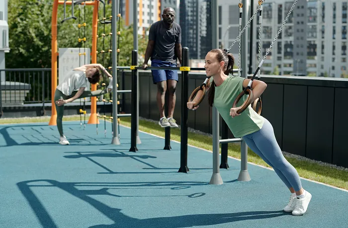 Adults using outdoor suspension rings and parallel bars on rooftop fitness area