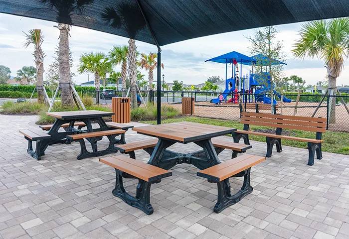 Picnic tables and bench under shade near playground, installed by Pro Playgrounds