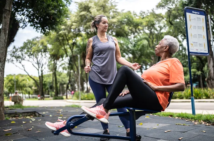 Two women using seated leg press machine at outdoor fitness park