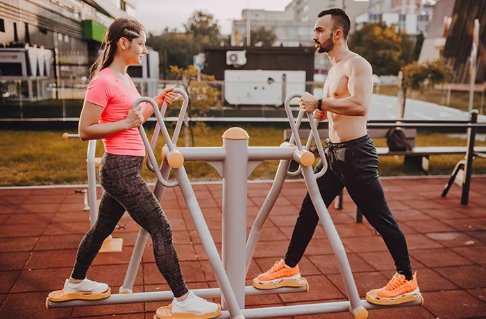 Man and woman using outdoor fitness equipment