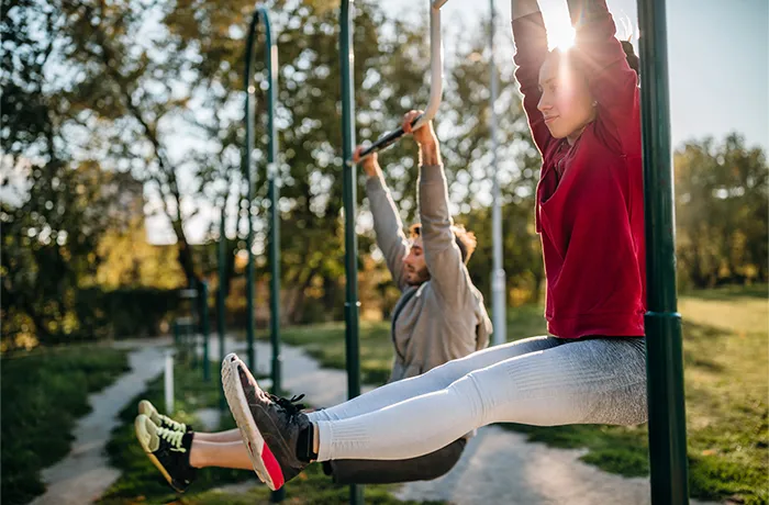 Two adults doing hanging leg raises on outdoor pull-up bars in park