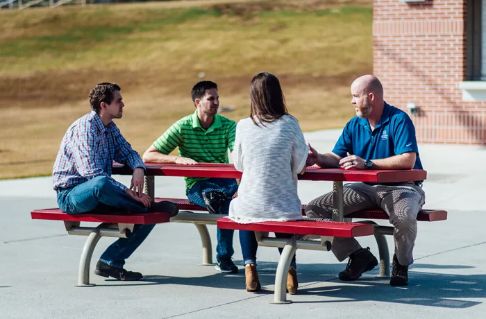 Red metal picnic table with four adults seated outdoors